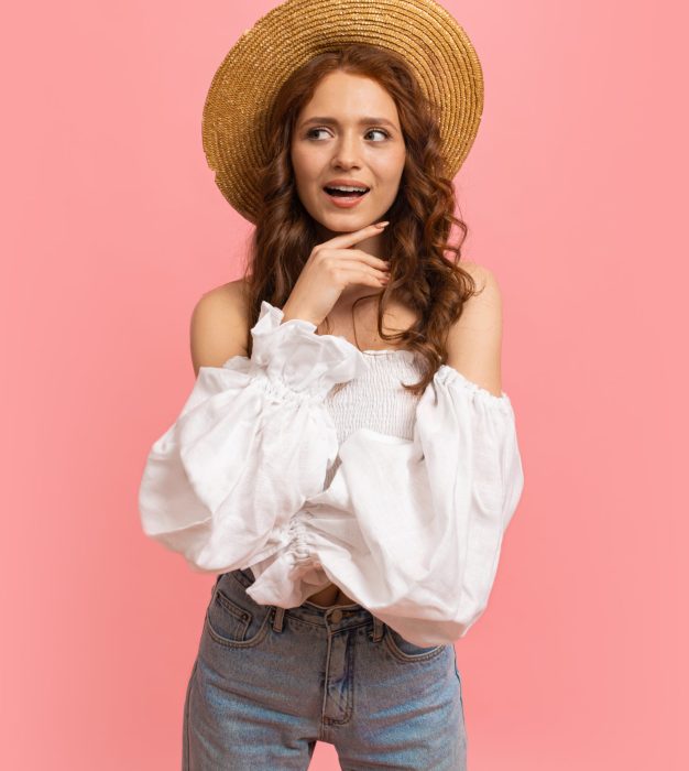 Summer studio portrait of  cheerful  red haired lady in fashionable outfit  having fun on pink background. Perfect wavy hairs.